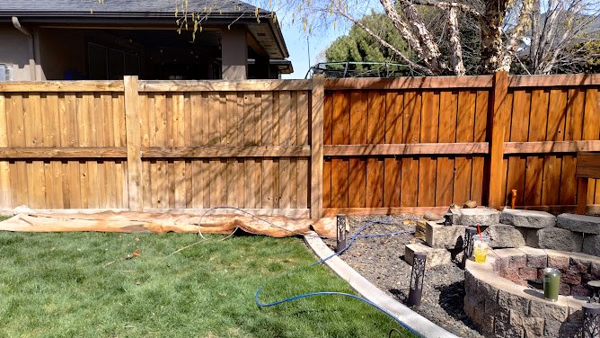 Hand applying stain to a wooden fence with a brush